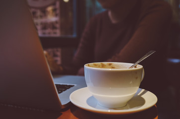 A young girl working with a cup of cappuccino coffee with laptop white screen on table. Royalty high quality free stock photo image of woman typing, working on laptop with a coffee cup in coffee shop
