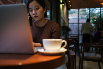 A young girl working with a cup of cappuccino coffee with laptop white screen on table. Royalty high quality free stock photo image of woman typing, working on laptop with a coffee cup in coffee shop