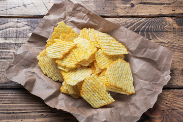 Potato fluted chips with spices on paper on a wooden table.