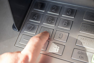 Hand entering PIN numbers on ATM bank machine