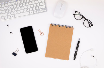 Top view office desk table with a silver computer keyboard, blank smartphone screen mockup, spiral notepad and supplies. The concept for mobile app screenshot