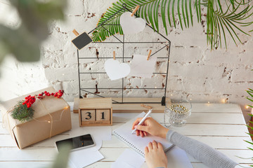 Writes wishes. Dreams of goals plans make a list for writing in notebook. Female hands on a background with wooden calendar, giftbox for New Year, winter holidays and Christmas time. Preparing