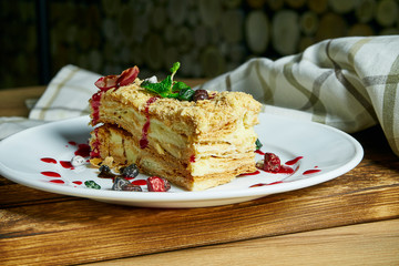 Close up view on cake Napoleon with berries and jam on white plate on wooden background. multi layered cake with pastry cream
