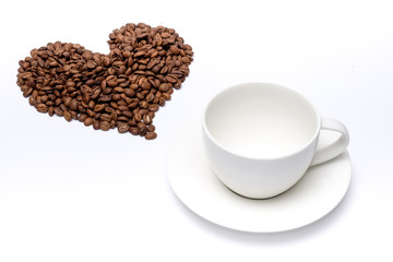 Coffee beans arrange into heart shape beside a cup on white background
