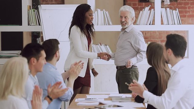 Old manager handshaking promoting happy african young worker at work