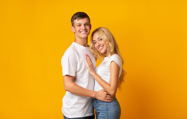 Portrait of young romantic couple cuddling on yellow background