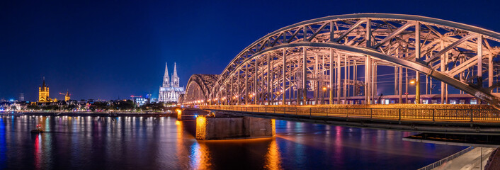 Night panorama of the illuminated Hohenzollern bridge over Rhine river. Beautiful cityscape of Cologne, Germany  with cathedral and Great St. Martin Church in the background