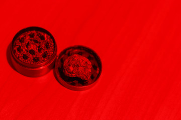 Close-up medicinal marijuana in a grinder on a table in red lighting. Drug use for medical purposes. Copy space