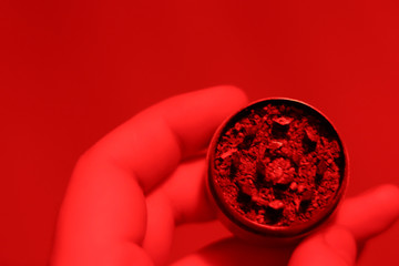 Close-up grinder with marijuana in hand. Top view. Red lighting. Copy space and blurred background. Medical drug use