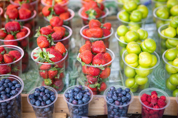 Different berries with multi colors sweet red and yellow and blueberry in plastic cups in market...