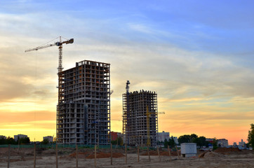 Fototapeta na wymiar Jib construction tower crane and new residential buildings at a construction site on the sunset and blue sky background - Image