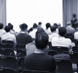 Speaker giving a talk at a corporate business conference. Audience in hall with presenter in front of presentation screen. Corporate executive giving speech during business and entrepreneur seminar. 