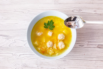 soup with meatballs in a white plate on a light wooden table