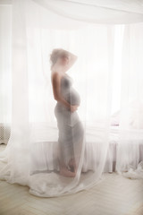 Fototapeta premium Kobieta w ciąży w sypialni z baldachimem biały. W ciąży blisko białego łóżka z bliska i kopia przestrzeń.