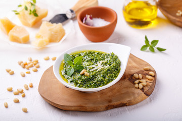 Pesto sauce with some ingredients - basil, olive oil, pine nuts, parmesan and garlic - on white table.