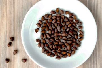 Pine nuts on white plate on wooden background. Healthy eating, organic food concept.