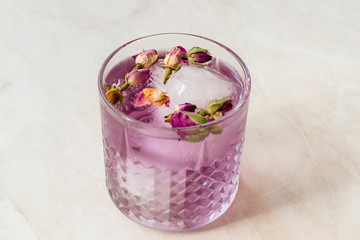 Pink Gin Tonic Cocktail with Dried Rose Buds and Ice in Glass Cup