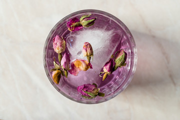 Obraz na płótnie Canvas Pink Gin Tonic Cocktail with Dried Rose Buds and Ice in Glass Cup