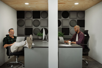 Two business entrepreneurs working in cubicle workstations in coworking office space, wide shot