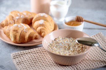 Oatmeal with milk, and croissants with honey on the table. Tasty breakfast.