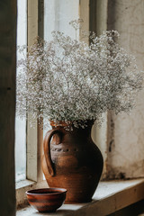 Beautiful retro still life with wild flowers in clay jug on windowsill of an old window.
