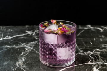 Pink Gin Tonic Cocktail with Dried Rose Buds and Ice in Glass Cup