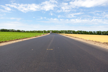 road in the countryside against a blue sky and white clouds surrounded by green grass