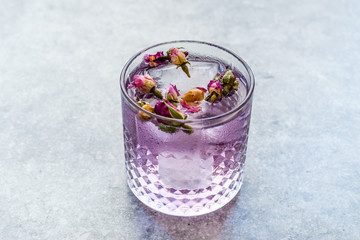 Fototapeta na wymiar Pink Gin Tonic Cocktail with Dried Rose Buds and Ice in Glass Cup