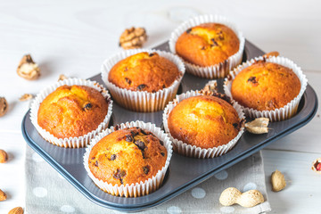 Vanilla caramel muffins in paper cups in bakeware on white wooden background