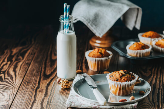 Vanilla caramel muffins in paper cups and bottles of milk on dark wooden background.