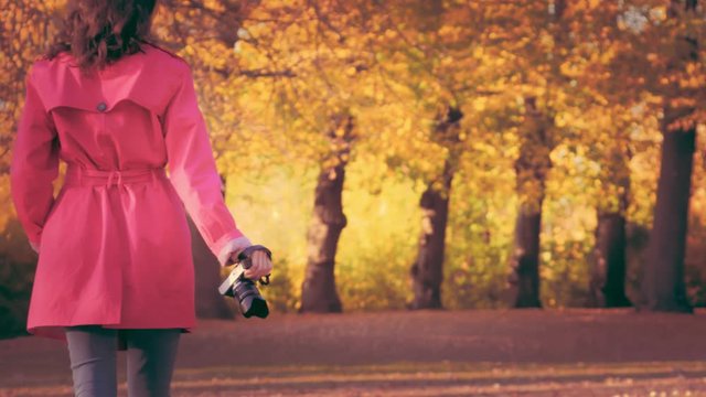 Young fashionable woman in Red cloak with camera in park in autumn.