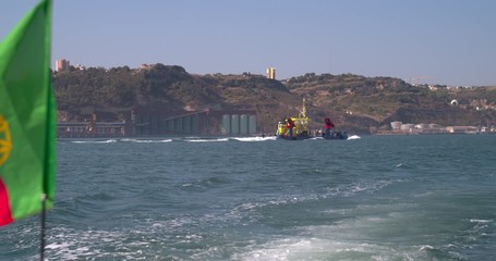 Yellow tugboat at river tejo (Lisbon, Portugal) with the Portuguese flag in the foreground. Slow motion shot - Powered by Adobe