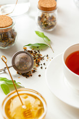 Cup of hot black tea on white table with dry tea jar
