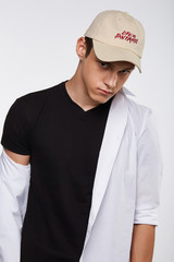 Cropped front view shot of a dark-haired man, wearing beige baseball cap with lettering 