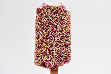 Ice cream on stick with colorful sprinkles over light background