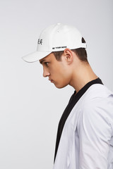 Cropped side photo of a dark-haired man, wearing white baseball cap with Chinese characters print and lettering 