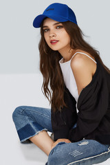 Full length shot of a dark-haired girl, sitting on a floor and wearing blue baseball cap with...