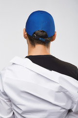 Cropped back view shot of a dark-haired man, wearing blue baseball cap with lettering 