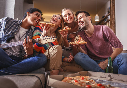 Group of friends making fun at the home party.They sitting in living room and eating pizza.