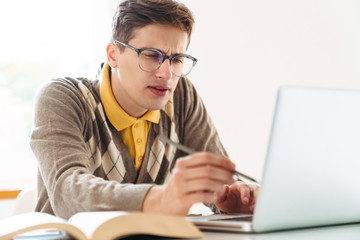 Guy student sit at the table indoors using laptop computer