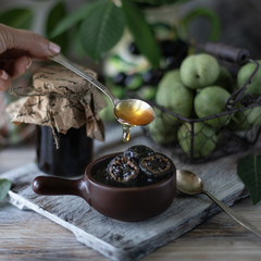 Jar of walnut jam on a wooden table and a group of green walnuts.