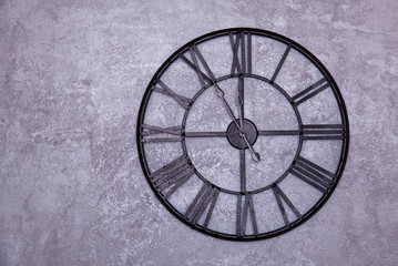 Vintage wall clock with roman numerals on the wall. gray stucco wall. Clock shows five to twelve...