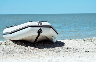 a rubber white boat stands alone on the seashore of blue water on the sand waiting for its owner a...