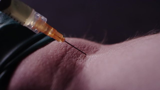 Close-up of a man shooting up heroin into his arm with a needle, blood drips out of his arm