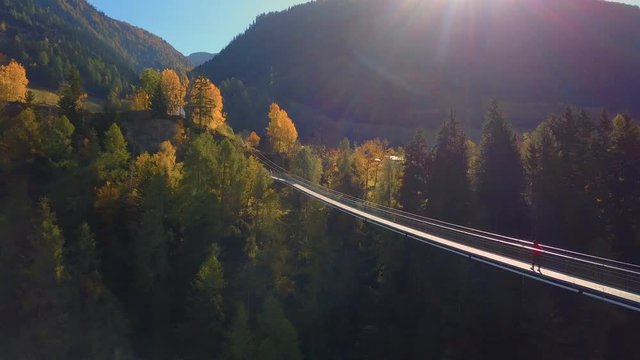 Man walks on hanging rope river bridge in forest
