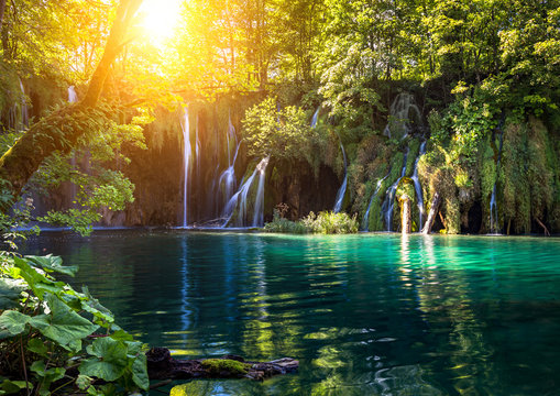 Idyllic waterfall scenery at famous Plitvice Lakes National Park as golden sunlight shimmers through leaves and illuminates beautiful cascades with scenic reflections on water, Lika-Senj, Croatia