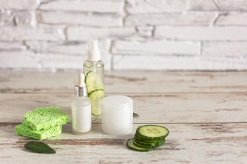 Bottles of homemade cucumber natural cosmetic with green cucumber slices and cotton-pads on wooden background.