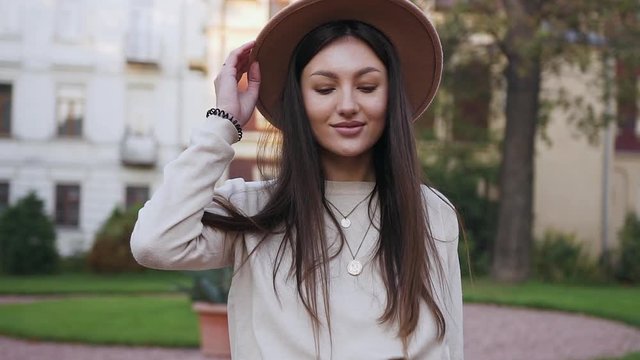 Joyful attractive 30-aged girl with trendy hat walking on the beautiful mansions background and looking at camera with nice smile