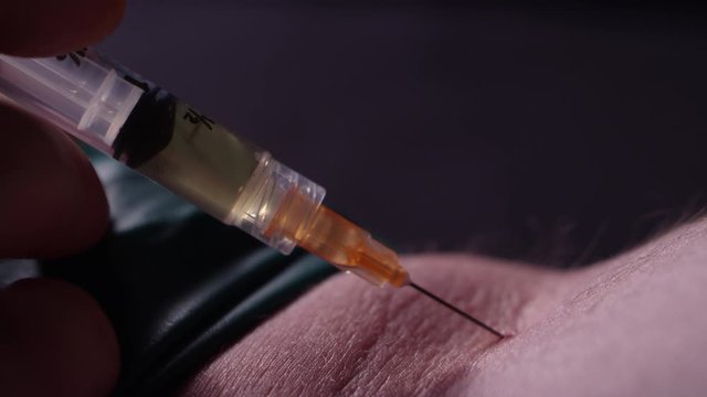 Close-up of a man shooting heroin into his arm with a needle and syringe in a dark room