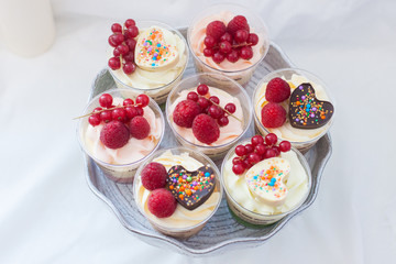 Assorted home made desserts in cups with whipped cream and fresh berries, strawberries, blueberries, raspberries, decorated with chocolate hearts. 